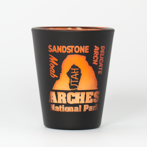 Black shot glass with orange text and Arches National Park design on a white background