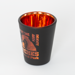 Black shot glass with orange interior and 'Delicate Arch' design on a white background