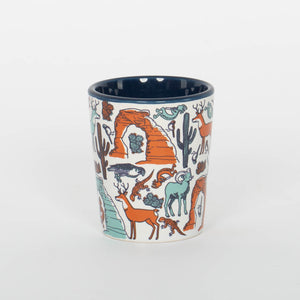 Ceramic mug with desert-themed design featuring animals and landscapes on a white background