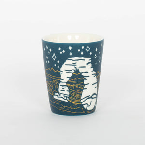 Ceramic mug with a design of a rock formation and starry sky on a blue background