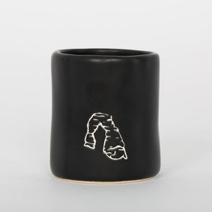 Black ceramic mug with a white line drawing on a light gray background