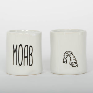 Two white ceramic mugs with 'MOAB' and a sandstone arch design on a white background