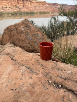 Red cup on a rock with a scenic background of a lake and cliffs.