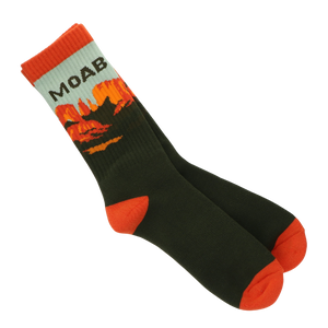 A pair of crew socks with a dark forest green body, bright orange toes and heels, and a light gray cuff featuring the text 'MOAB' above an orange and yellow mountain landscape graphic, shown on a plain white background.