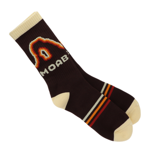 A pair of dark brown crew socks with cream-colored heels, toes, and cuffs, featuring a large knit 'MOAB' logo and a red, orange, and yellow arch graphic on the side.