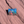 Square Arches enamel pin with Bigfoot and a green raptor beside Delicate Arch under a blue sky, lying on red sandstone in Moab, Utah.