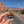 Hand holding the Arches National Park hexagon sunset enamel pin on a road through the Moab red rock cliffs.