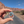 Hand holding the Arches National Park oval badge enamel pin on a road through the Moab red rock cliffs.