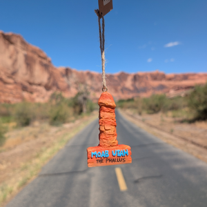 Bert Anderson Collection Moab Utah Phallus Ornament, a red rock tower ornament hanging on twine with a Moab desert road behind