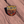Shield shaped Dead Horse Point enamel pin showing the Colorado River gooseneck below the overlook, lying on red sandstone in Moab, Utah.