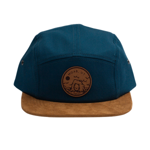 Locale Camper Leather Patch Cap, a navy five panel cap with a tan suede brim and round Moab leather patch, angled view