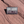 Gray and maroon Moab Utah 1902 enamel pin with Delicate Arch above diagonal stripes, lying on red sandstone in Moab, Utah.