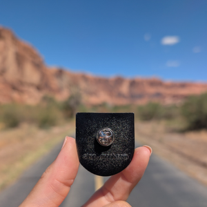 Back of the Moab Utah sunburst enamel pin showing the rubber clutch and simplymoab.com stamp.