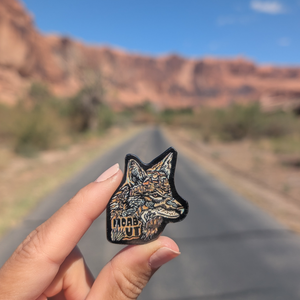 Hand holding the Moab UT wolf enamel pin on a road through the Moab red rock cliffs.