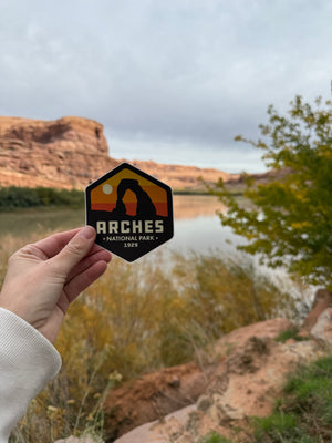 Hand holding the Simply Moab Arches Hexagon Sunrise Sticker by the Colorado River near Moab