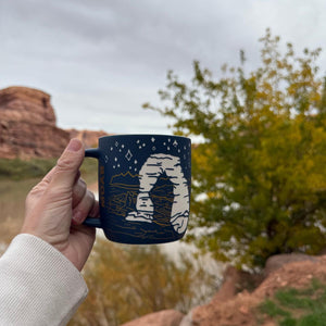 Hand holding the Smith-Western Arches Etched Siren Mug outdoors by red rocks near Moab